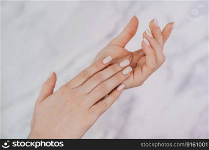Beautiful female hands with french manicure on nails. Soft skin, skincare, beauty treatment concept. Young woman applying cream or lotion onto graceful hands with slender fingers on light background. Female hands with french manicure on nails. Soft skin, skincare, beauty