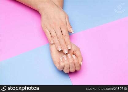 Beautiful Female Hands with French manicure over colorful paper background.. Beautiful Female Hands with French manicure over colorful paper background