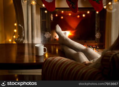 Beautiful female legs in woolen stockings warming up at fireplace