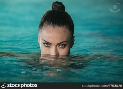 Beautiful female looking at camera while swimming in clean water of pool in spa salon. Woman swimming in pool