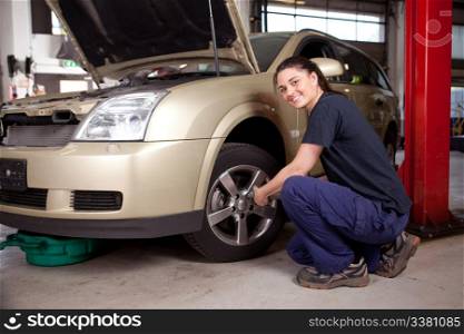 Beautiful female mechanic changing tire on car