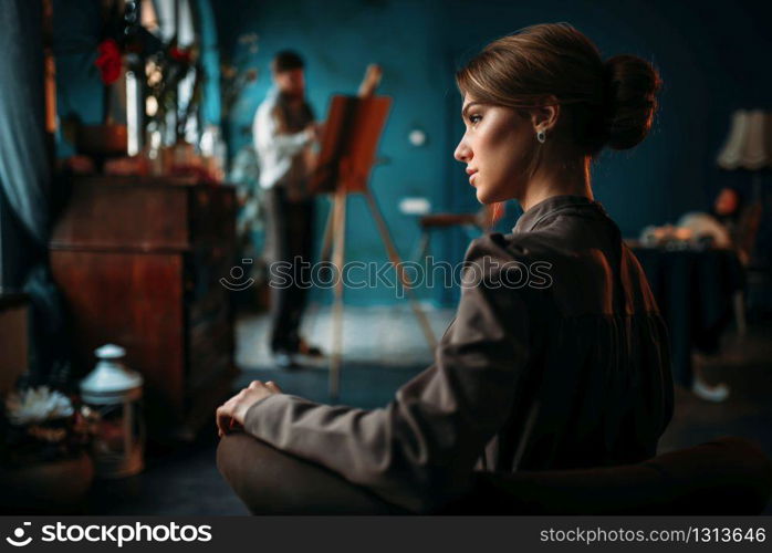 Beautiful female poseur, painter against easel on background. Oil paint