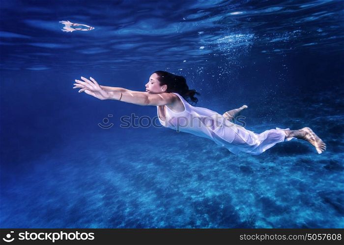 Beautiful female swimming underwater, wearing long white dress, fashion life, active lifestyle, summer vacation concept