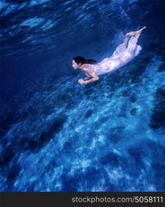 Beautiful female swimming underwater, wearing long white dress, fashion life, active lifestyle, summer vacation concept