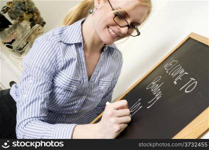 Beautiful Female Teacher Writes a Message on ChalkBoard Saying Welcome to Biology