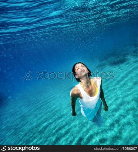 Beautiful female wearing white dress underwater, active lifestyle, swimming in clear transparent water of sea, summer vacation concept