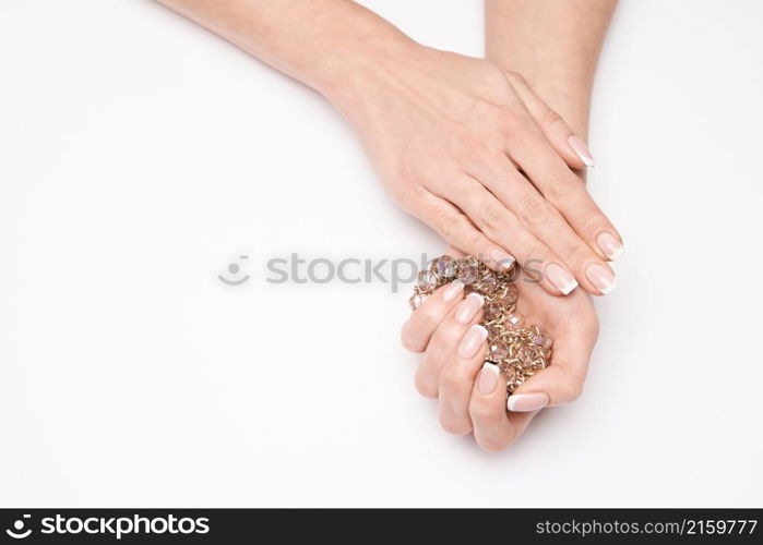 Beautiful Female well-groomed Hands with French manicure holding necklace over light background.. Beautiful Female well-groomed Hands with French manicure holding necklace over light background