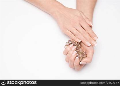 Beautiful Female well-groomed Hands with French manicure holding necklace over light background.. Beautiful Female well-groomed Hands with French manicure holding necklace over light background
