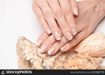 Beautiful Female well-groomed Hands with French manicure holding sea shell over light background.. Beautiful Female well-groomed Hands with French manicure holding sea shell over light background