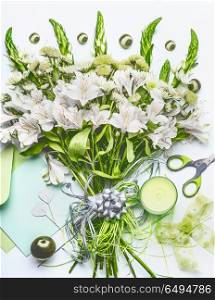 Beautiful festive bouquet with green flowers on white desk background with envelope and paper card mock up, ribbon, candle and scissors, top view. Holidays greeting concept, flat lay