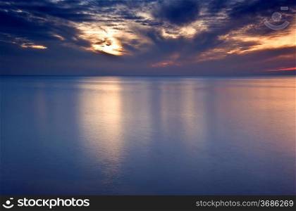 Beautiful fiery glow sunset reflected in smooth long exposure sea with fluffy repeating pattern clouds