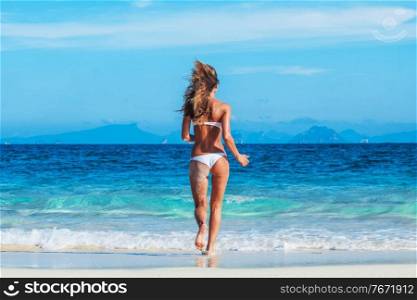 Beautiful fit woman in bikni run into tropical sea. Woman run into sea