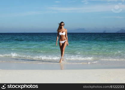 Beautiful fit woman in bikni walking from sea to tropical beach. Woman walk to beach