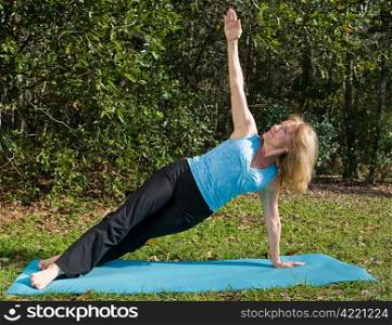 Beautiful fit woman in her sixties doing the side staff yoga asana, outdoors in a natural setting.