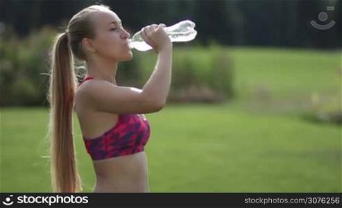 Beautiful fitness woman drinking water after work out exercising outside in the park and smiling at camera