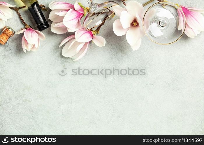 Beautiful flat lay with spring magnolia flowers, wine and glasses on grey stone background, top view, copy space