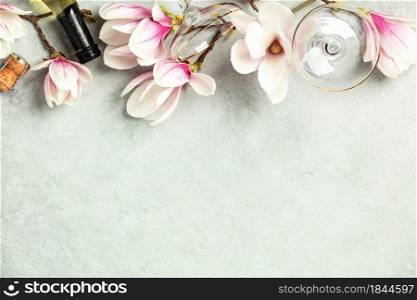 Beautiful flat lay with spring magnolia flowers, wine and glasses on grey stone background, top view, copy space