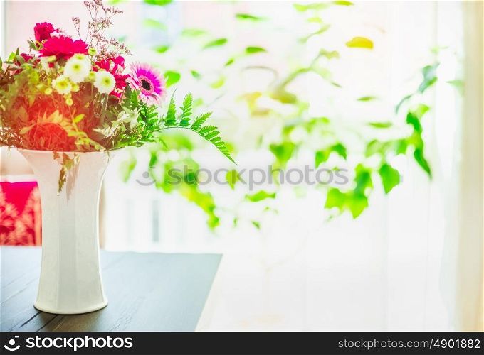 Beautiful flowers bunch in white vase on table at window background with green leaves, indoor