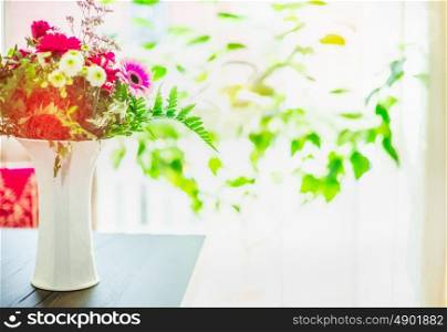 Beautiful flowers bunch in white vase on table at window background with green leaves, indoor