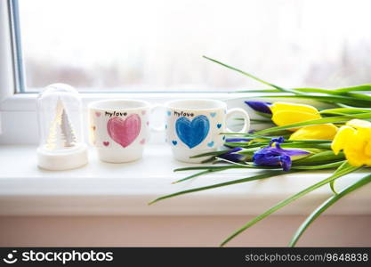 beautiful flowers-tulips and irises lie on the windowsill with two cups of coffee.. beautiful flowers-tulips and irises lie on the windowsill with two cups of coffee