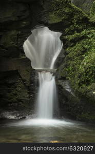 Beautiful flowing waterfall with magical fairy tale feel in lush green forest setting