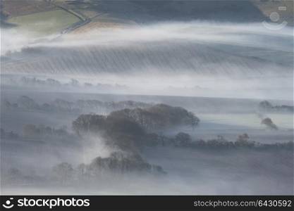 Beautiful foggy English countryside landscape at sunrise in Winter with layers rolling through the fields
