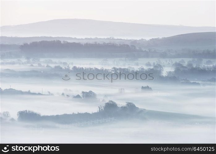 Beautiful foggy English countryside landscape at sunrise in Winter with layers rolling through the fields