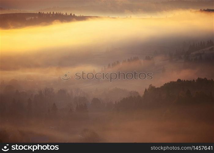 Beautiful foggy landscape in the sunrise mountains. Fantastic morning foggy autumn hills glowing by sunlight.