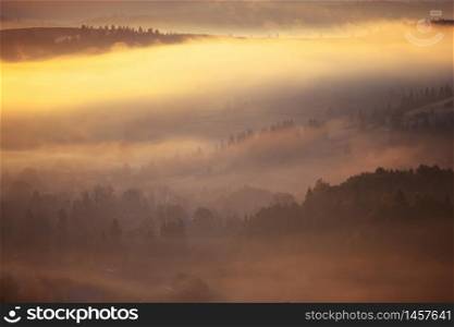 Beautiful foggy landscape in the sunrise mountains. Fantastic morning foggy autumn hills glowing by sunlight.