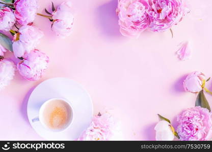 Beautiful fresh pink and white peony fresh flowers on pink table with cup of coffee, frame with copy space for your text, top view and flat lay background, toned. Fresh peony flowers