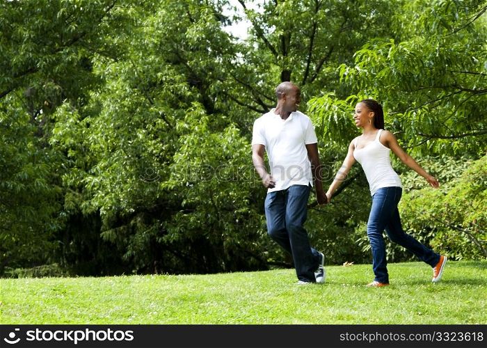Beautiful fun happy smiling African American young couple running playing in park, wearing white shirts and blue jeans.