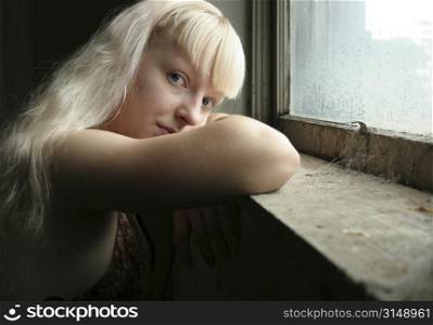 Beautiful German seventeen year old girl with head on window sill. Spiderwebs in window. Natural beauty - no make-up. Blonde hair, blue eyes.
