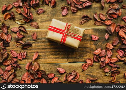 Beautiful gift with a heart around dry red petals on a rustic wood