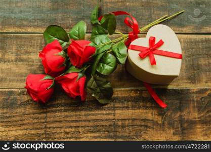 Beautiful gift with heart shape with a bouquet of red roses on a wood background