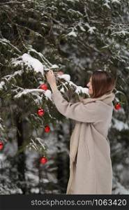 beautiful girl decorates the Christmas tree with red balls in the forest. winter wood. Winter. Merry Christmas.. beautiful girl decorates the Christmas tree with red balls in the forest. winter wood. Winter. Merry Christmas