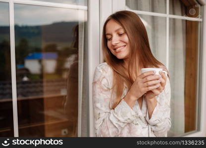 beautiful girl drinking coffee on the balcony. Portrait of a happy woman thinking and looking away at breakfast on vacation with a resort or hotel on the mountain in the background.. beautiful girl drinking coffee on the balcony. Portrait of a happy woman thinking and looking away at breakfast on vacation with a resort or hotel on the mountain in the background