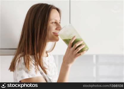 Beautiful girl drinks freshly prepared smoothie in kitchen. smoothies freshly made from assorted vegetable ingredients on kitchen counter. Healthy Eating. selective focus.. Beautiful girl drinks freshly prepared smoothie in kitchen. smoothies freshly made from assorted vegetable ingredients on kitchen counter. Healthy Eating. selective focus