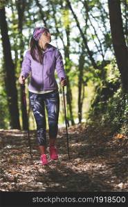 Beautiful girl during a hike with Nordic walking practice in the woods. After smart working