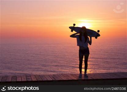Beautiful girl holding a skateboard with the sunset in the background