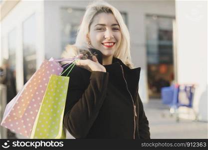 Beautiful girl holding shopping bags, looking at camera and smiling while sitting on a bench