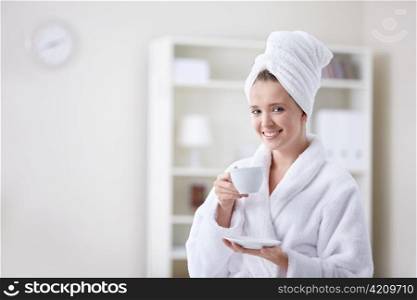 Beautiful girl in a bathrobe and a towel keeps the cup