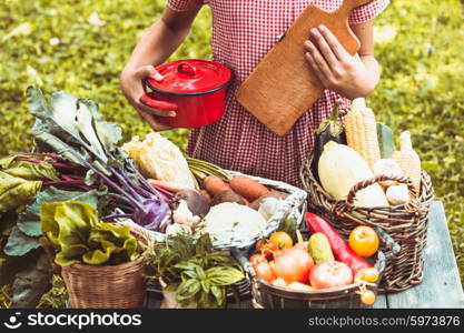 Beautiful girl in a checkered dress plays with a variety of vegetables on the lawn. Lovely girl plays with vegetables