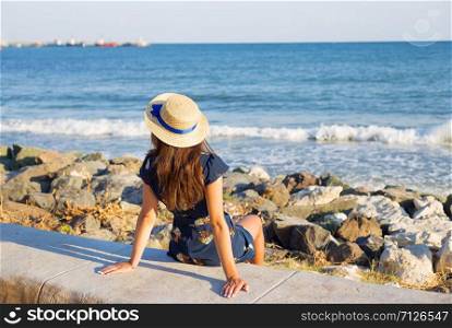 Beautiful girl in a hat sits near the sea on stones.. Beautiful girl in a hat sits near the sea on stones