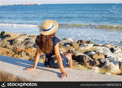 Beautiful girl in a hat sits near the sea on stones