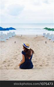 Beautiful girl in a hat sits with her back on a sandy beach.. Beautiful girl in a hat sits with her back on a sandy beach