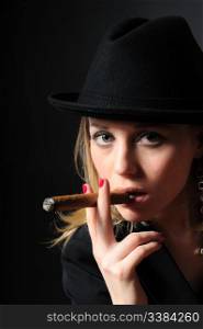 Beautiful girl in a hat smoking a cigar on a black background looks into the camera
