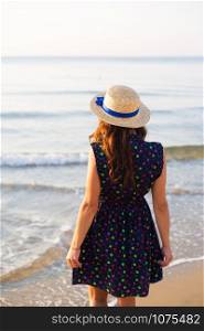 Beautiful girl in a hat stands with her back on a sandy beach. Beautiful girl in a hat stands with her back on a sandy beach.