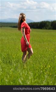 Beautiful girl in a red dress in a field on a sunny day
