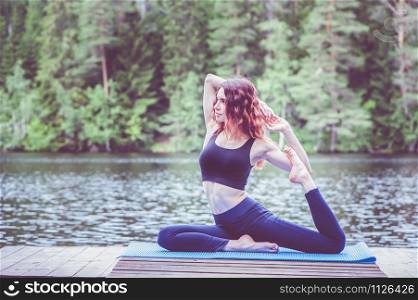 Beautiful girl in a yoga pose on the lake. Eka Pada Rajakapotasana . One Legged King Pigeon Pose . The concept of peace, healthy lifestyle