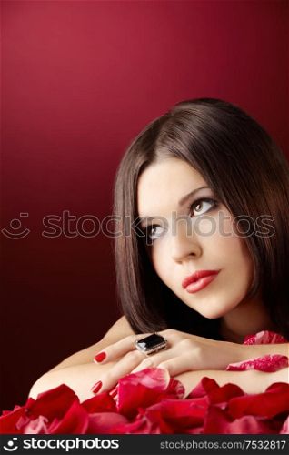 Beautiful girl in an environment of petals of the red roses, isolated